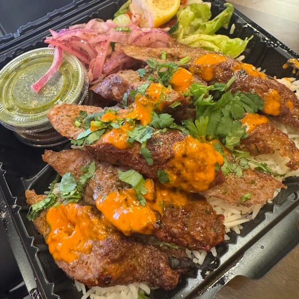 Indian seekh kebab with orange sauce and cilantro, served with rice, pickled onions, and salad.