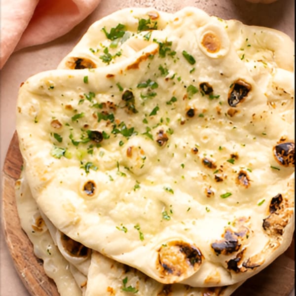 A stack of freshly baked Indian naan bread, garnished with green herbs, on a wooden board.