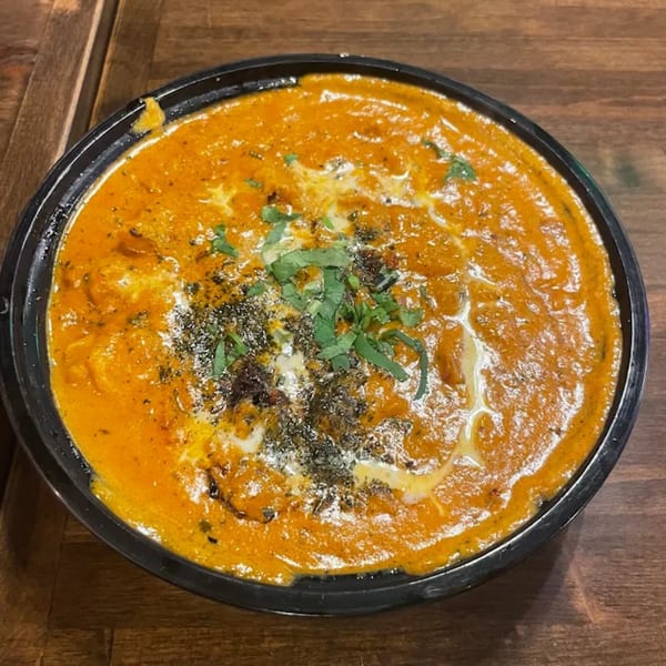 Close-up of Indian butter chicken curry with cream and herbs in a black bowl.
