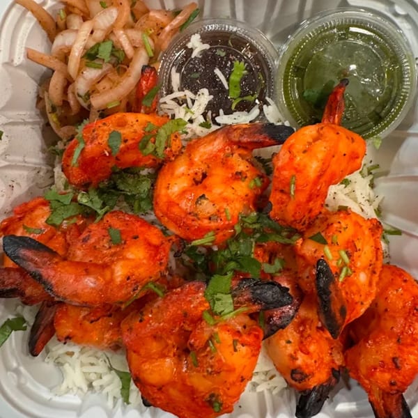 Tandoori shrimp with rice, pickled onions, and two sauces in a white takeout container.