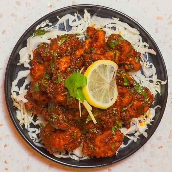Indian chicken dish with a rich red sauce, garnished with cilantro, ginger, and a lemon slice.